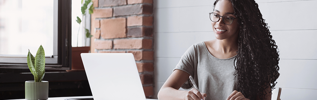 Woman writing while looking at laptop